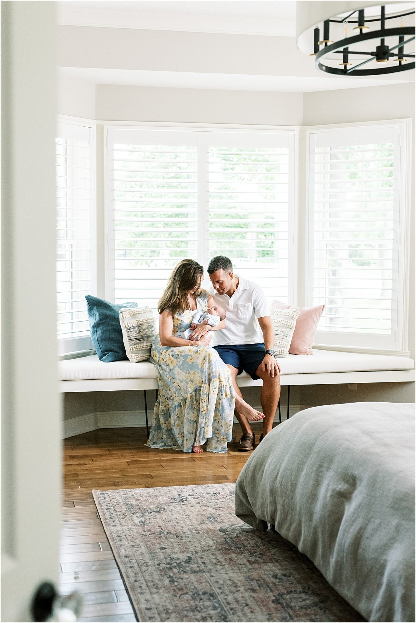 In-home lifestyle session with parents in master bedroom. Parents are holding their newborn son. Photo by Lindsay Konopa Photography.