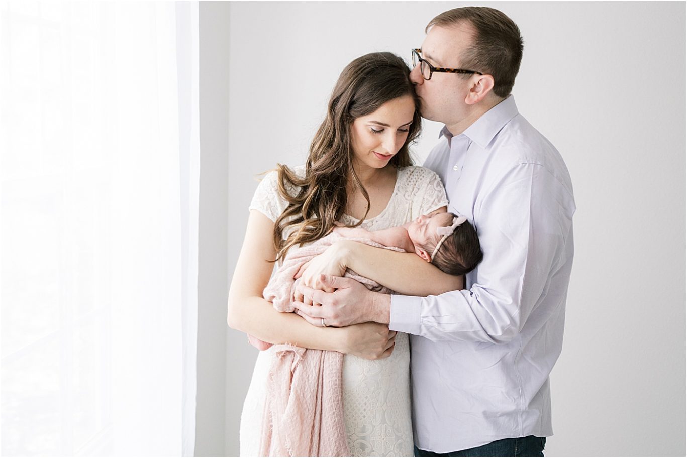 Dad kissing Mom while holding their baby girl. Newborn photo by Lindsay Konopa Photography.