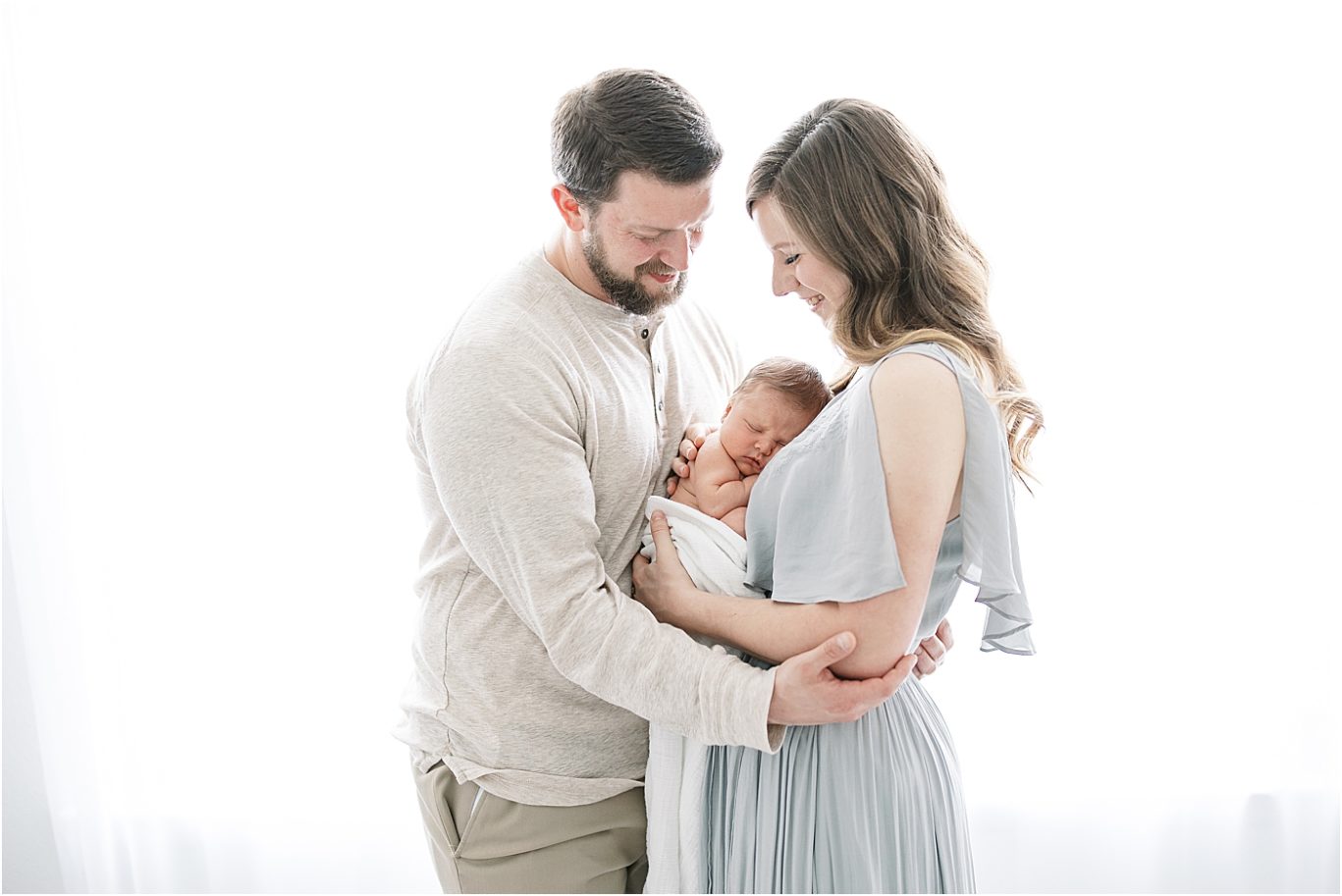 Backlit photo of new parents holding their baby boy in studio for newborn photos. Photo by Lindsay Konopa Photography.
