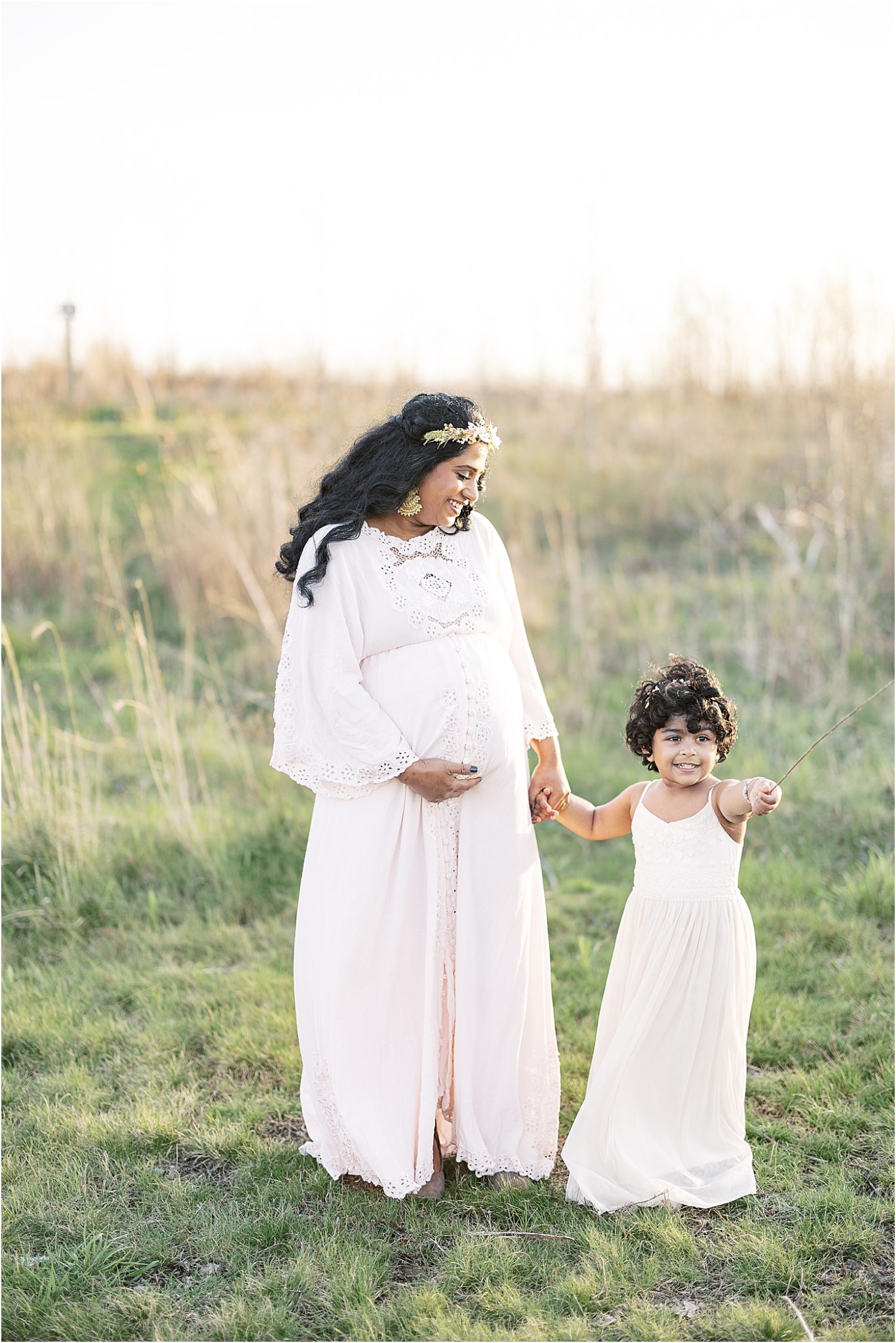 Mom walking with her daughter through field during maternity photoshoot. Photo by Lindsay Konopa Photography.