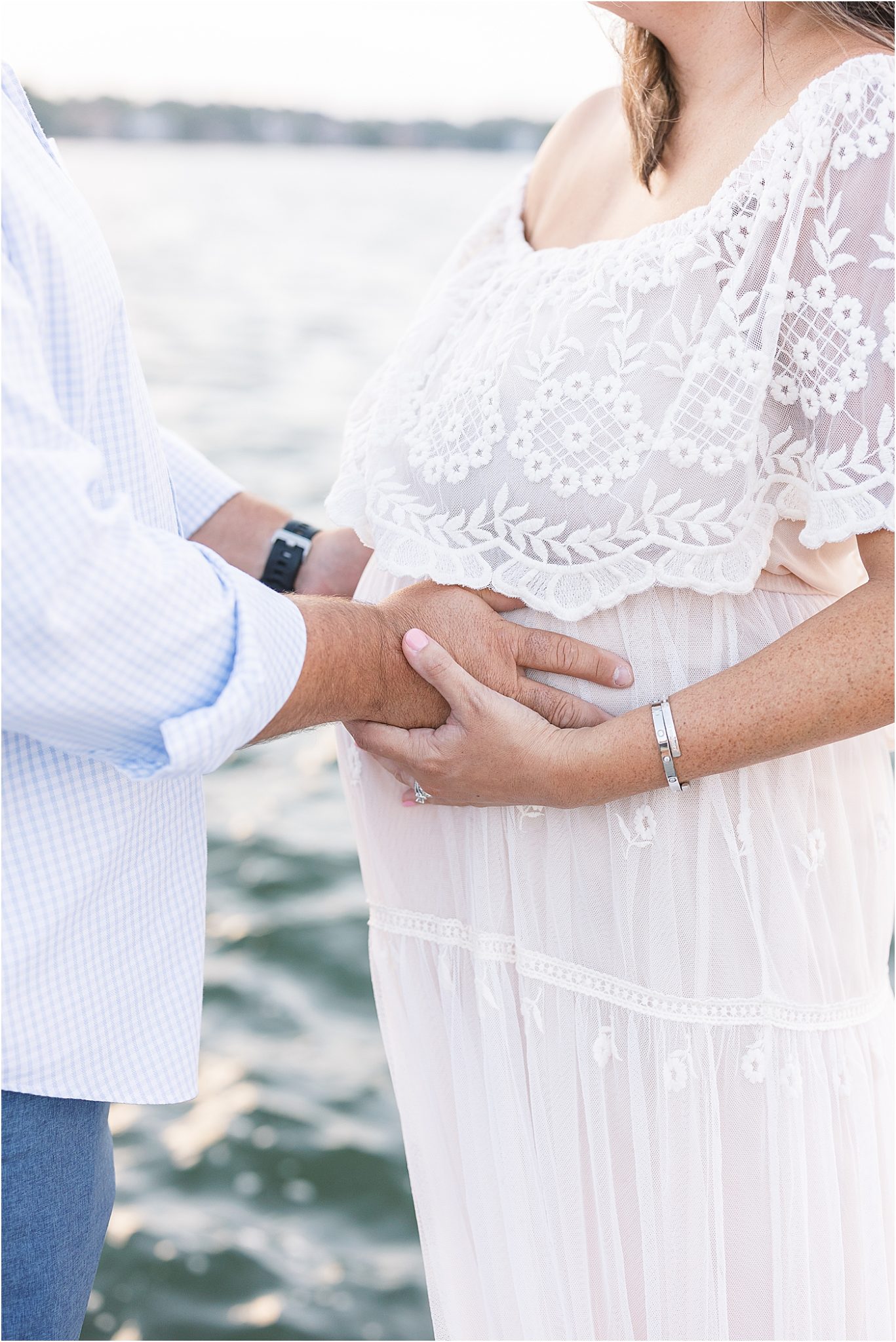 Dad with hands on Moms pregnant belly overlooking the water | Lindsay Konopa Photography