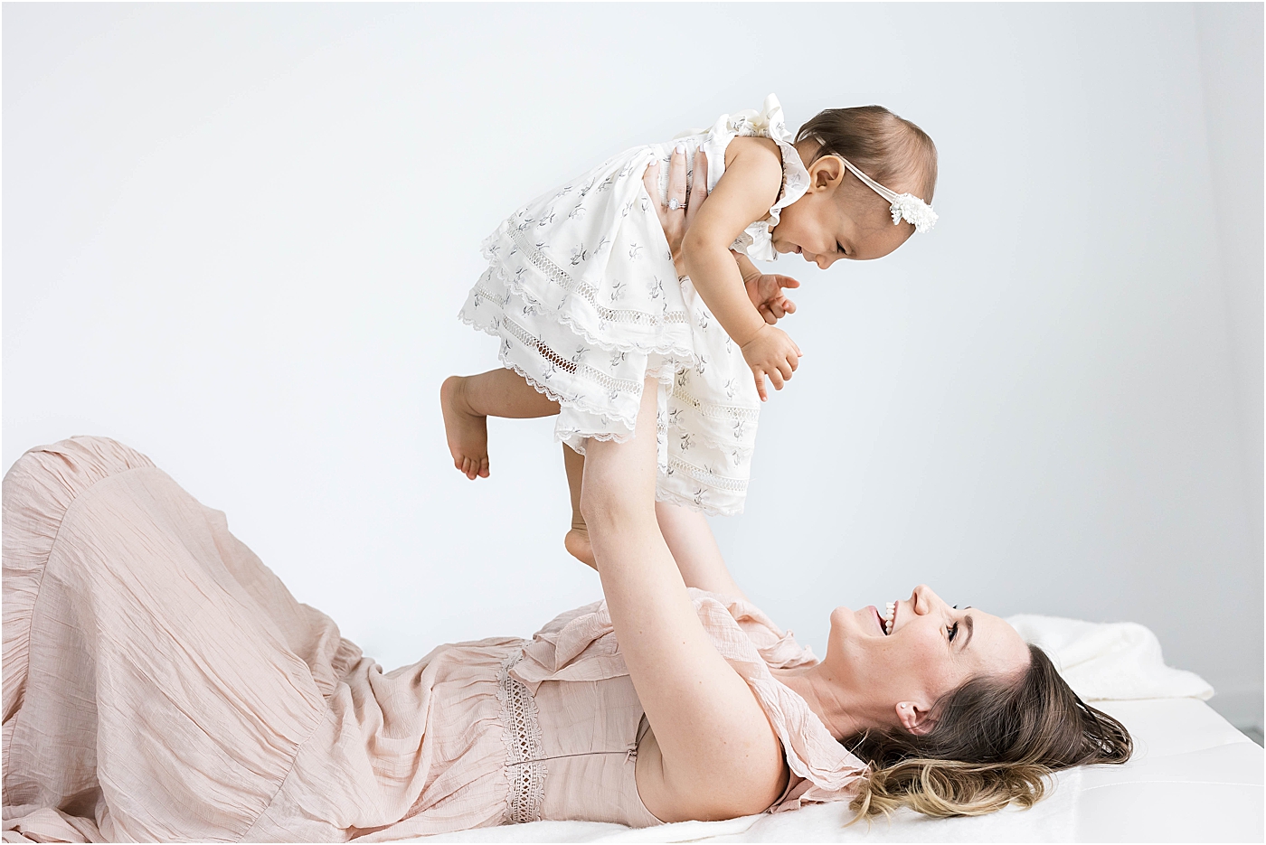 Mom laying on bed holding daughter up above her | Lindsay Konopa Photography