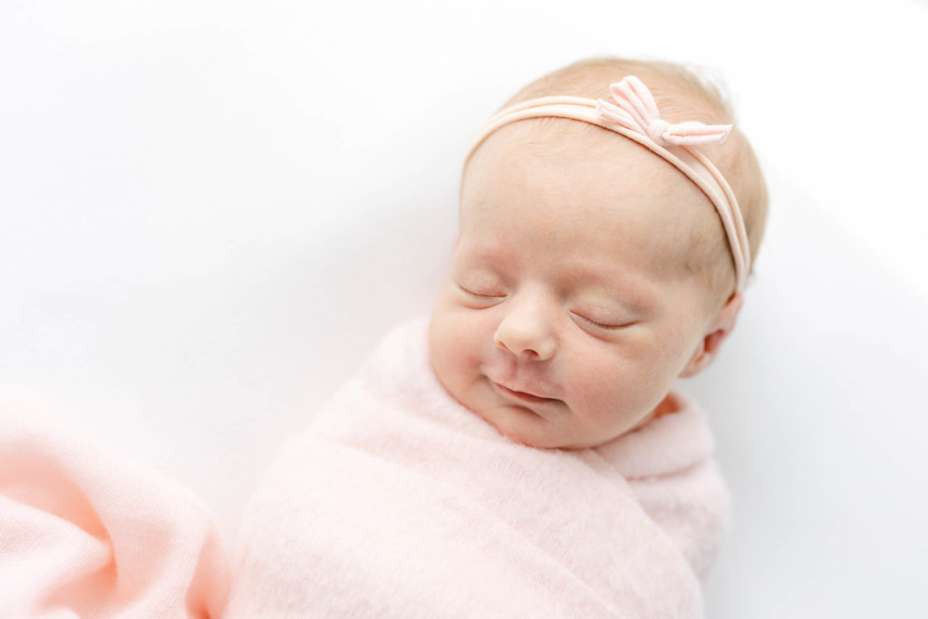 When to schedule your newborn session. A newborn baby in a pink blanket sleeping peacefully.