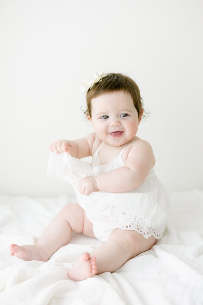 A sweet baby girl giggles and plays with her white dress in Lindsay Konopa Photography's studio.