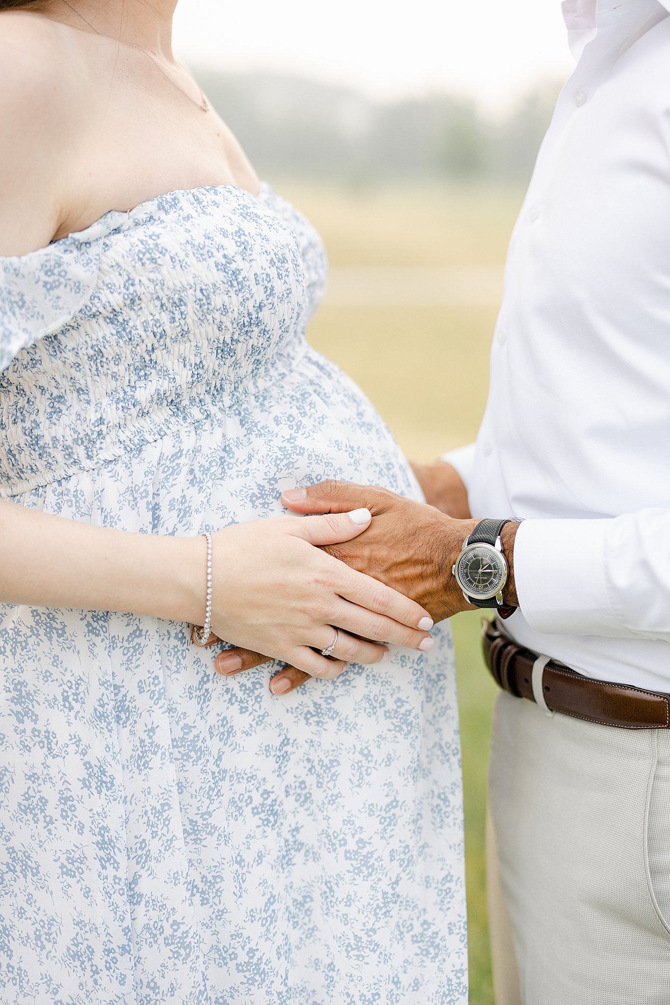 Details of expecting parents standing in a field holding the bump after some Indianapolis prenatal yoga