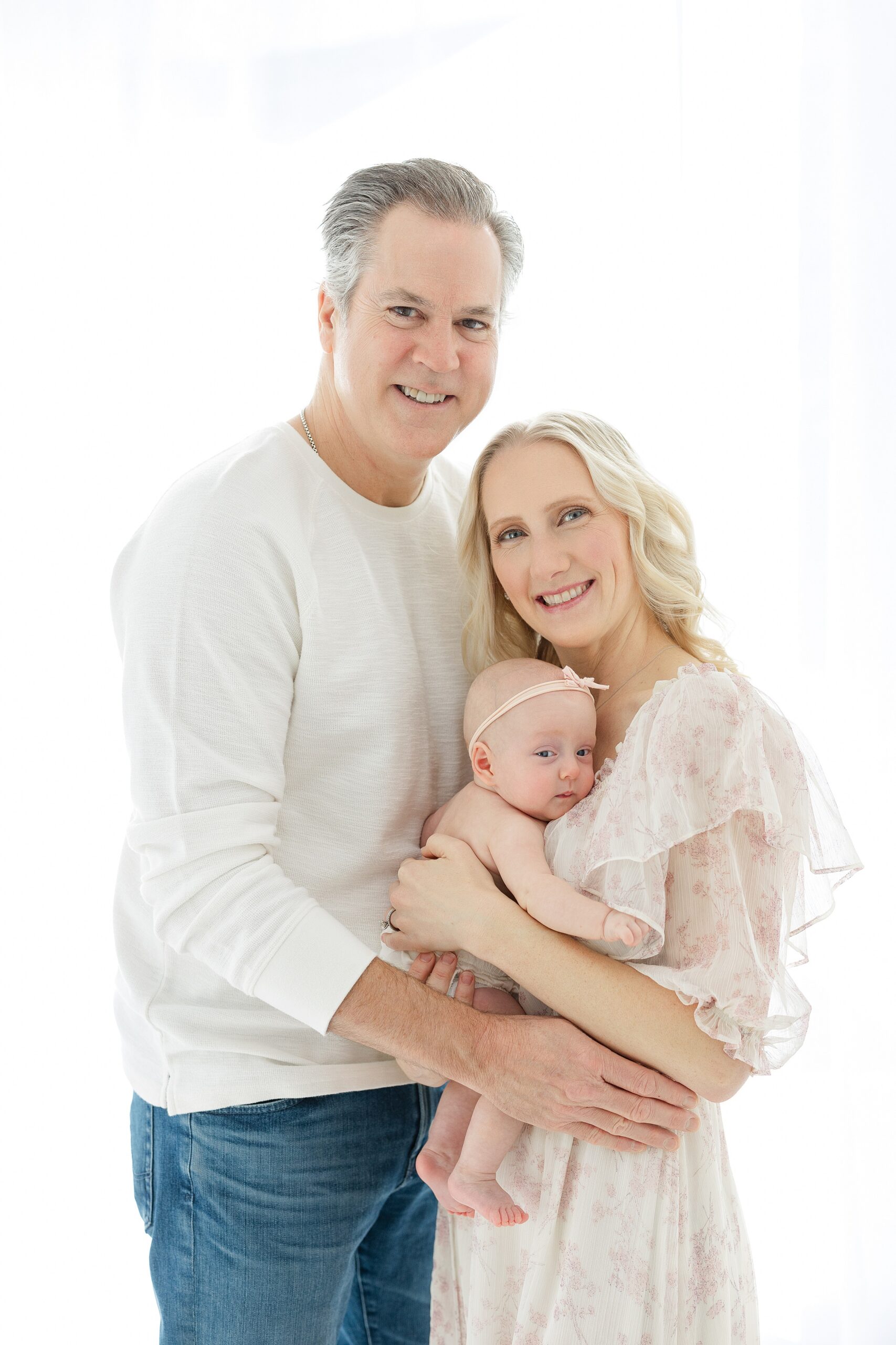 Happy new parents stand in a studio window holding their newborn baby daughter