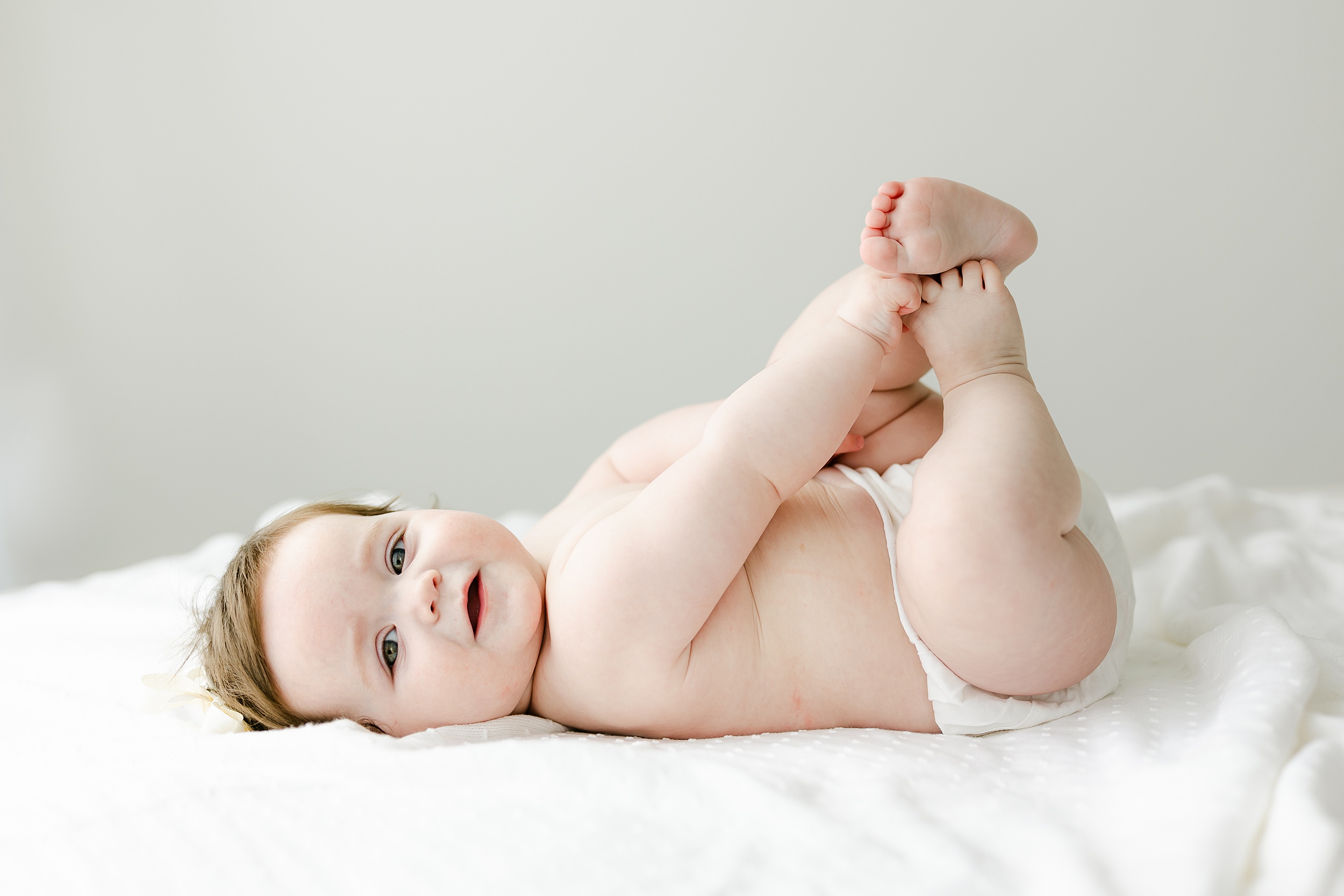A happy infant lays on a bed playing with it's feet in the air