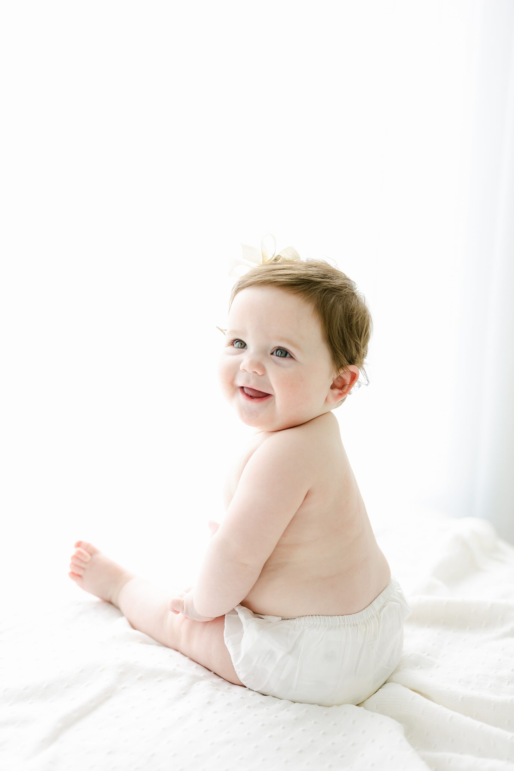 A happy infant sits on a bed under a bright window smiling after visiting a pediatric chiropractors Indianapolis
