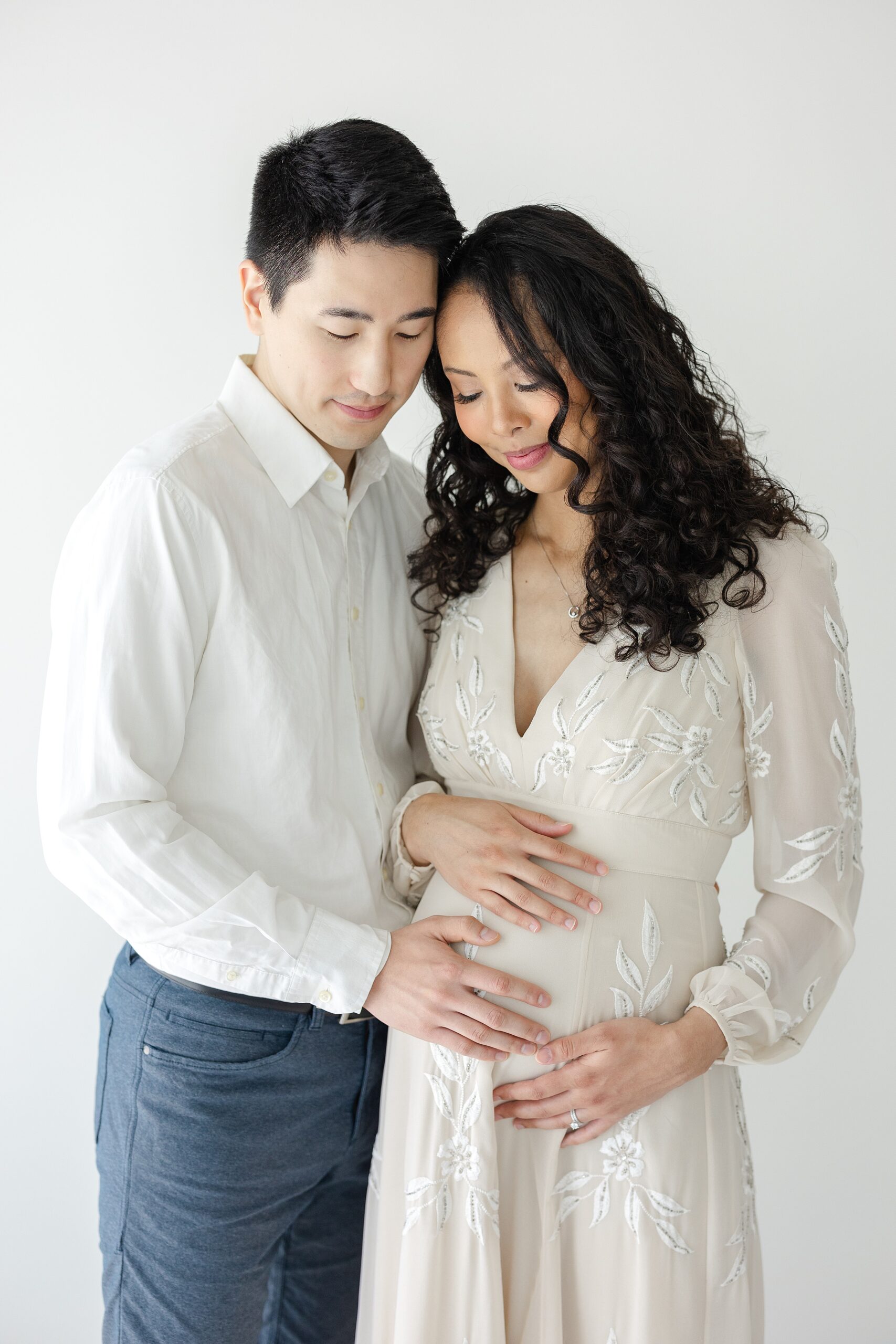 Happy expecting parents snuggle while standing in a studio and holding the bump before visiting Prenatal Chiropractors in Indianapolis