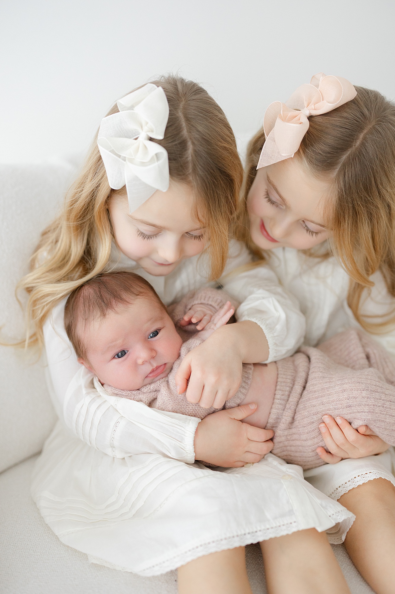 Two big sisters hold their baby sister during a light and airy newborn session in Carmel, Indiana
